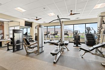 A large fitness room with cardio equipment and large windows